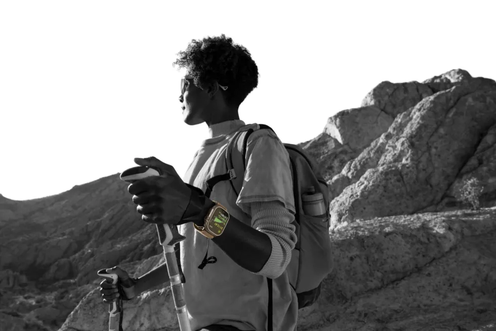 A person hiking in the mountains with poles and a backpack, wearing Apple Watch Ultra